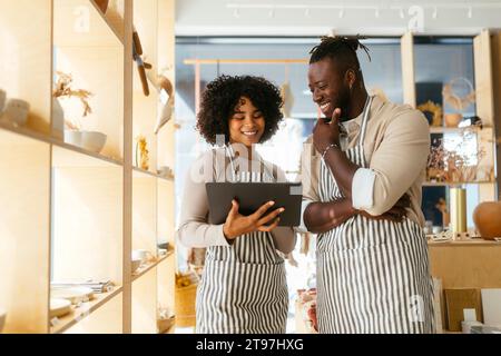 Lächelnder Besitzer mit einem Kollegen, der einen Tablet-PC im Geschäft hält Stockfoto