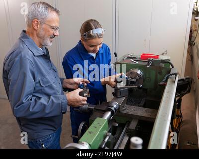 Der Trainee arbeitet mit dem Ausbilder, der in der Werkstatt in der Nähe der Drehmaschine steht Stockfoto