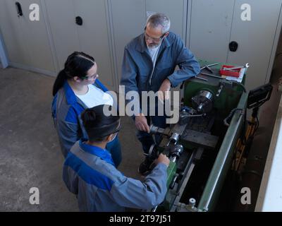 Kursleiter bespricht mit Auszubildenden, die in der Werkstatt in der Nähe der Drehmaschine stehen Stockfoto