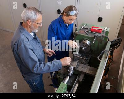 Schulungsleiter unterrichtet den Trainee in der Werkstatt mit Drehmaschine Stockfoto