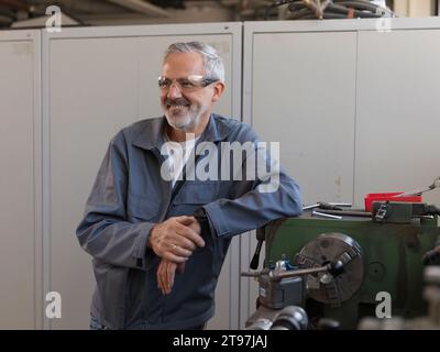 Lächelnder Arbeiter, der sich in der Werkstatt auf die Drehmaschine lehnt Stockfoto