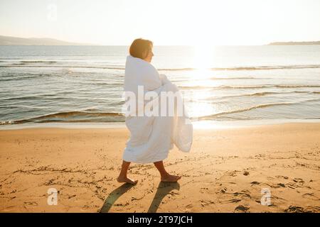 Frau in Decke gehüllt, barfuß auf Sand am Strand Stockfoto