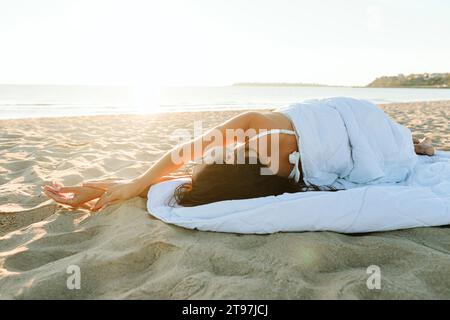 Frau mit erhobenen Armen, in Decke gewickelt, am Strand gelegen Stockfoto