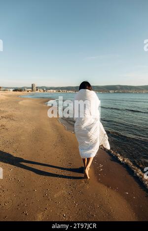 Frau in Decke gehüllt, die am Strand auf Sand läuft Stockfoto