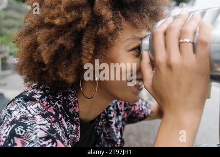 Glückliche junge Frau, die durch Münzferngläser schaut Stockfoto