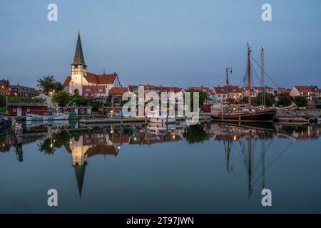 Dänemark, Bornholm, Ronne, St. Nikolaus Kirche und umliegende Häuser spiegeln sich in der Abenddämmerung im Küstenwasser Stockfoto