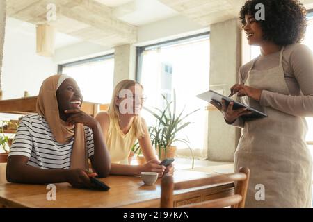 Lächelnde Kellnerin, die Bestellungen von Kunden über einen Tablet-PC im Café entgegennimmt Stockfoto