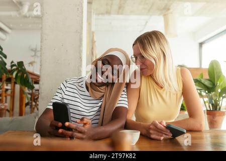 Lächelnde Frau, die einem Freund im Café ihr Smartphone zeigt Stockfoto