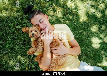 Lächelnder Mann, der Hund hält und im Park auf Gras liegt Stockfoto