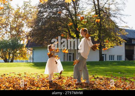 Glückliche Mutter und Tochter spielen mit Herbstlaub vor dem Haus Stockfoto