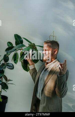 Glücklicher Geschäftsmann mit geschlossenen Augen, Meditation und balancierende Metallpyramide auf dem Kopf vor der Wand Stockfoto