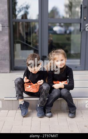 Geschwister sitzen auf dem Bürgersteig und halten Körbe für Halloween-Süßigkeiten Stockfoto