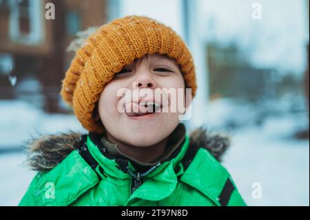 Verspielter Junge, der warme Kleidung trägt und im Winter die Zunge herausstreckt Stockfoto