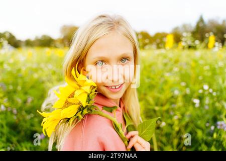Lächelndes blondes Mädchen, das Sonnenblume auf dem Feld hält Stockfoto
