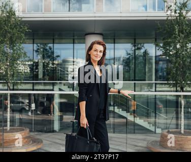 Seitenansicht einer selbstbewussten Geschäftsfrau mittleren Alters mit Tasche, die vor einem Bürogebäude steht Stockfoto