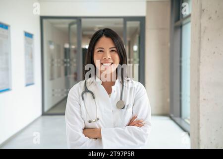 Glücklicher Arzt, der mit überkreuzten Armen im Krankenhaus steht Stockfoto