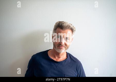 Lächelnder reifer Mann vor der weißen Wand Stockfoto