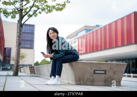 Lächelnde Geschäftsfrau, die mit Smartphone auf dem Sitz sitzt Stockfoto