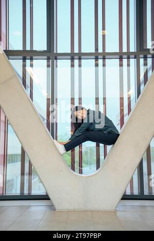 Lächelnde Geschäftsfrau, die auf einer architektonischen Säule sitzt Stockfoto