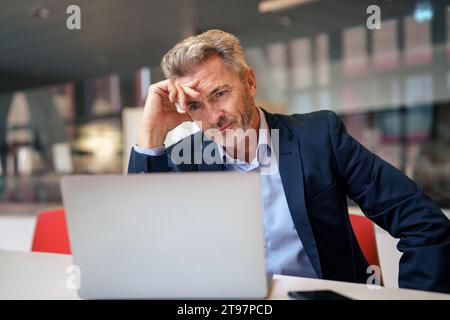 Gestresster, reifer Geschäftsmann, der am Tisch in der Cafeteria einen Laptop benutzt Stockfoto