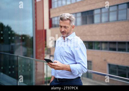 Geschäftsmann, der sein Smartphone in der Nähe des Geländes auf dem Balkon benutzt Stockfoto