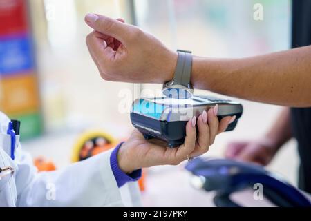 Hand des Kunden, der per Tap-to-Pay-Methode über Smart Watch in der Apotheke bezahlt Stockfoto