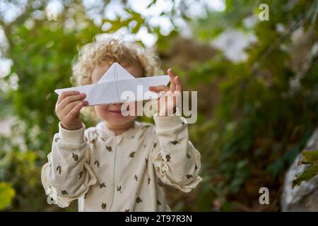 Glückliches Mädchen, das das Papierboot vor dem Baum hält Stockfoto