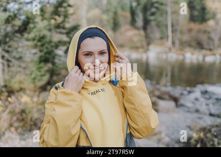 Lächelnde Frau mit Kapuzenhemd im Wald Stockfoto