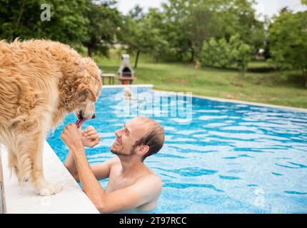 Glücklicher Mann streichelt Golden Retriever Hund und genießt im Schwimmbad Stockfoto