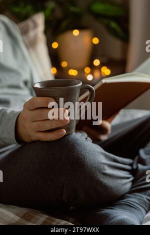 Ein weißer Mann, der sich zu Hause entspannt, ein Buch liest, Kaffee im Bett trinkt Stockfoto