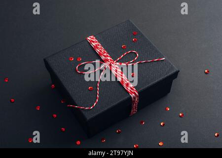 Geschenk in einer schwarzen Box und rotem Konfetti auf schwarzem Hintergrund. Weihnachtskonzept. Draufsicht. Stockfoto