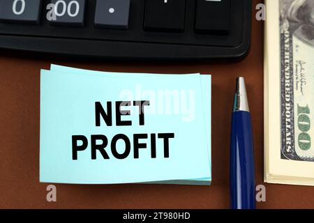Geschäftskonzept. Auf einer braunen Oberfläche liegen ein Taschenrechner, Dollars, Stifte und Aufkleber mit der Aufschrift - Net Profit Stockfoto