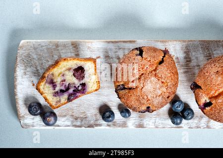 Hausgemachte große Blueberry Muffins serviert auf einer Holzplatte. Einer der Muffins wird halbiert, mit einem gleichmäßigen Aufstrich Heidelbeeren durch den Kuchen Stockfoto