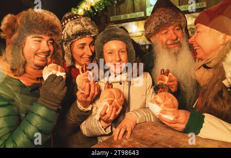 Familie genießt Würstchen auf einem Weihnachtsmarkt und lächelt zusammen mit Winterhüten Stockfoto