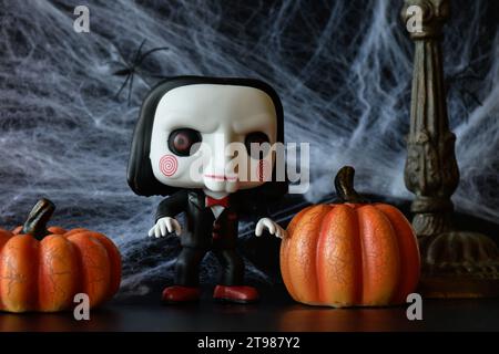 Funko Pop Actionfigur von Billy der Puppe aus dem beliebten Slasher-Horrorfilm SAW. Halloween-Deko, Spinnennetz, Kürbisse, düstere, gruselige Saison. Stockfoto