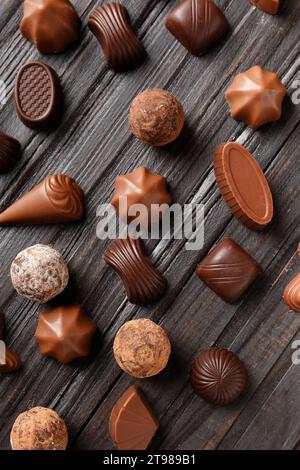 Verschiedene Schokoladenbonbons auf dunklem Holzhintergrund, Draufsicht. Verschiedene Süßigkeiten auf dem Tisch. Dunkle Schokolade und Milchschokolade. Schokoladendessert. Stockfoto