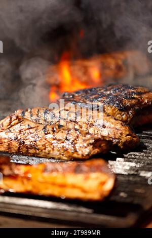 Appetitliche saftige Tomahawk-Steaks, Ribeye und Lendensteaks auf einem Grill über brennender Flamme beim Grillen. Gegrilltes Fleisch in einem Restaurant. Stockfoto