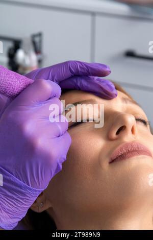 Beauty Master macht permanentes Augenbrauen-Make-up in einem Schönheitssalon. Hände eines Kosmetologen, der die Augenbrauen mit Mikroblase vertreibt. Tätowierung auf das Gesicht. Stockfoto