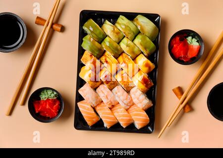 Ein Set von hellen mehrfarbigen Sushi-Rollen mit Garnelen, Lachs, Avocado in Plastikverpackung, chinesischen Essstäbchen, Soße, Ingwer auf hellem Hintergrund, Stockfoto