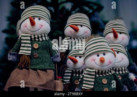 Eine Gruppe von Schneemännern mit roten Möhrennasen in grünen Pullover, Tüchern und gestreiften Hüten unter dem Weihnachtsbaum. Weihnachtsdekoration. Stockfoto