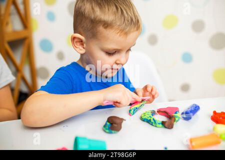 Der kleine Junge spielt begeistert mit Plastilin, spielt Teig auf weißem Tisch Stockfoto