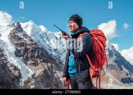 Porträt eines Sherpa-Mannes mit Rucksack, der Walkie-Talkie benutzt, um einen Rettungshubschrauber mit Mera Peak 6476 m Hintergrund zu rufen. Expedition im hohen Himalaya DURIN Stockfoto