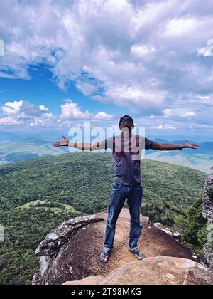 Ein Mann mit Silhouette steht auf einem Berg und genießt den atemberaubenden Blick auf die umliegende Landschaft Stockfoto