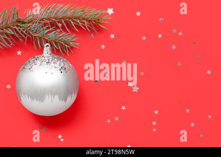 Komposition mit silberner Weihnachtskugel und Tannenzweig auf rotem Hintergrund mit Glitzern Stockfoto