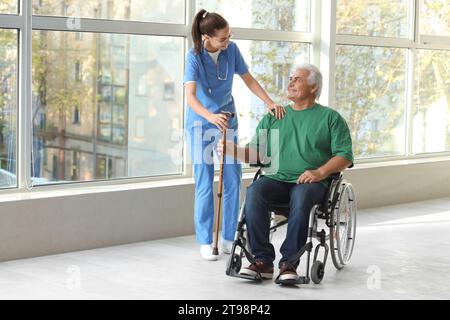 Seniorenmann im Rollstuhl mit Stock und Krankenschwester im Krankenhaus Stockfoto