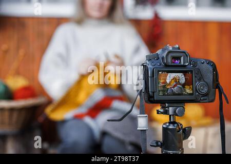 Frau nimmt auf Kamera Video Tutorial oder Blog über Stricktechnik Wolle auf. Influencer Lehren und E-Learning online Stockfoto