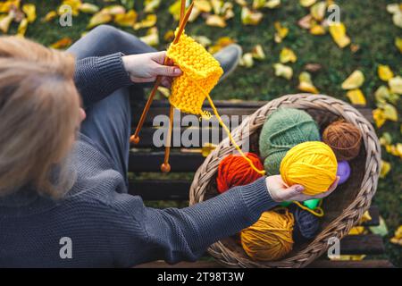 Warme Kleidung aus Garn stricken. Frau, die einen gelben Wollball aus dem Korb wählt. Entspannen Sie sich auf der Bank im Herbstpark Stockfoto