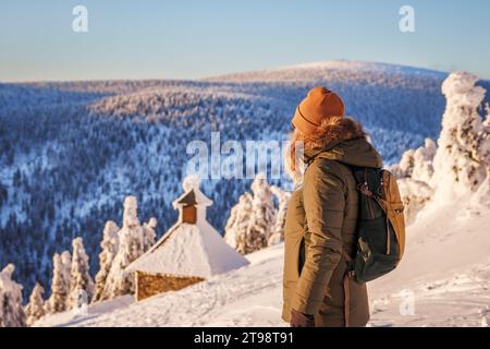 Frau wandert im Winter in den Jeseniky Bergen. Weibliche Touristen, die vom Gipfel aus eine wunderschöne Schneelandschaft sehen, kennt sich als Red Mountain aus Stockfoto