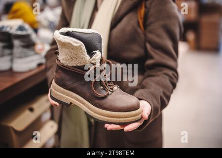 Frau wählt und kauft Winterstiefel aus Leder im Schuhgeschäft. Trendige Schuhe kaufen Stockfoto