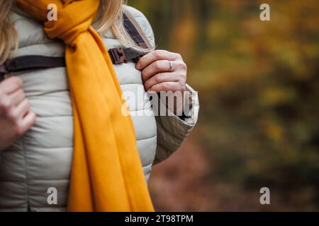 Sportbekleidung für kaltes Wetter. Frau mit Rucksack wandert im Herbstwald und trägt Jacke und Schal Stockfoto